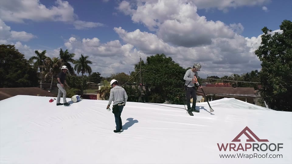 Wraproof crew finishing a membrane install on a residential roof under a clear sky